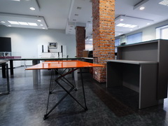 Оранжевый обеденный стол перегороворв с дизайнерскими металлическими опорами в выставочном зале