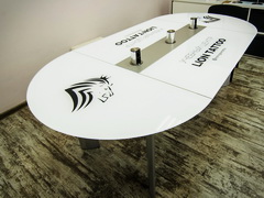 Стол переговоров из белого стекла, с оргинальными металлическими опорами, встроенными розетками и нанесенным логотипом на столешницу